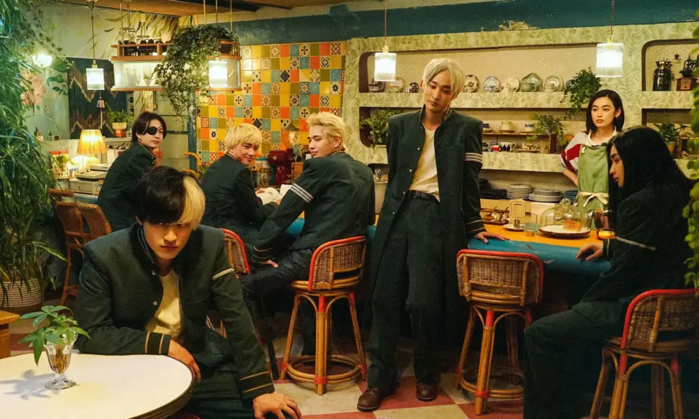 Six students in green uniforms lounge in a retro tiled cafe as a waitress watches