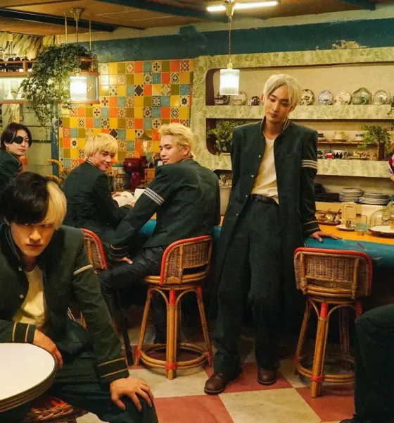 Six students in green uniforms lounge in a retro tiled cafe as a waitress watches